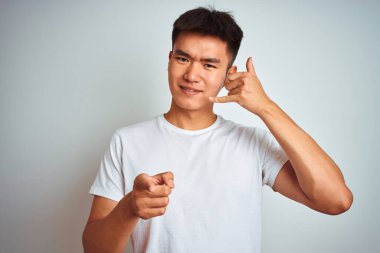 Asyalı genç adam tişörtünü giyip beyaz arka planda dikiliyor gülümsüyor telefonda konuşuyor ve seni işaret ediyor. Ara beni..
