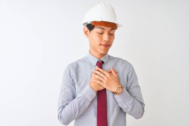 Kravat ve miğfer takan Çinli mimar izole edilmiş beyaz arka plan üzerinde duruyor elleri göğsünde, gözleri kapalı ve yüzünde minnet dolu bir jest ile gülümsüyor. Sağlık kavramı.