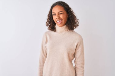 Balıkçı yaka kazak giyen genç Brezilyalı kadın izole edilmiş beyaz arka planda durmuş kameraya seksi bir ifadeyle bakıyor, neşeli ve mutlu bir yüzle..