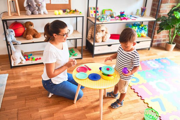 Beautiful toddler boy sitting on puzzle playing with plastic plates, fruits and vegetables at kindergarten