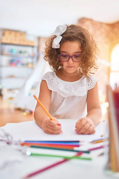 幼稚园漂亮的幼儿 戴着眼镜 坐着画画 用的是纸和铅笔 — 图库照片