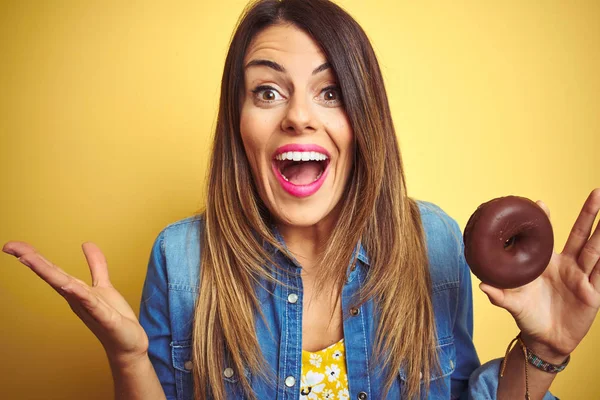 Sarı Arka Planda Çikolatalı Çörek Yiyen Genç Güzel Bir Kadın — Stok fotoğraf