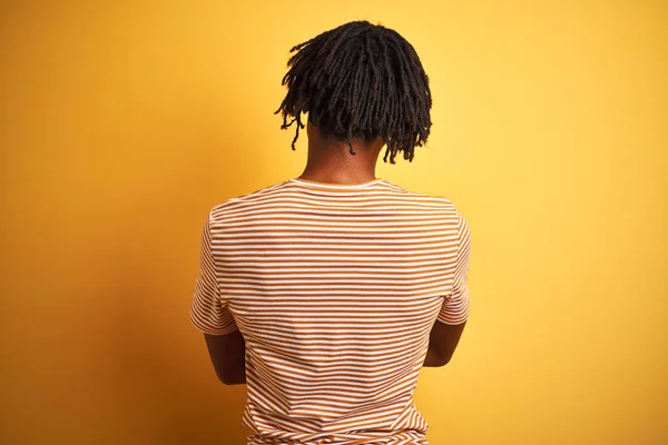 穿着条纹T恤衫站在孤立的黄色背景上 背向后站着 交叉着双臂向外看去的黑人 — 图库照片