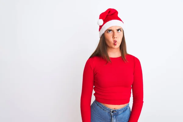 孤立した白い背景の上に立ってクリスマスサンタの帽子を身に着けている若い美しい女の子は 狂気とコミカルなジェスチャーで魚の顔を作る 面白い表現 — ストック写真