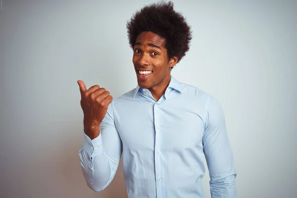 Young african american man with afro hair wearing elegant shirt over isolated white background smiling with happy face looking and pointing to the side with thumb up.