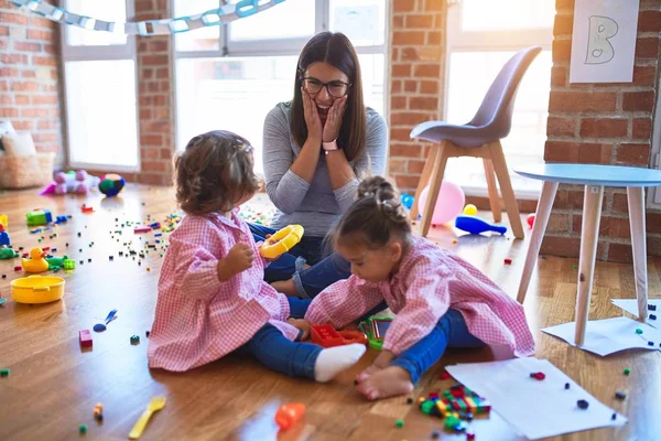 Young beautiful teacher and toddlers wearing uniform building pyramid using hoops at kindergarten