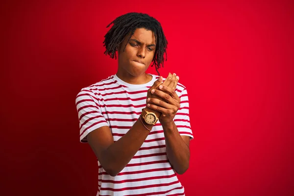 孤立した赤い背景の上に立つストライプのTシャツを身に着けているドレッドロックを持つ若いアフロ男手や指の痛み 関節炎の炎症 — ストック写真