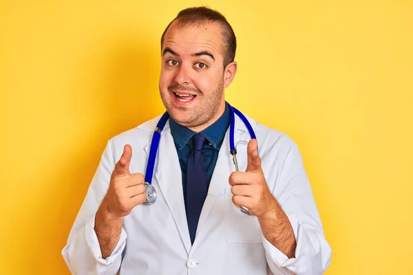 身穿外套和听诊器的年轻医生站在孤立的黄色背景上 手指指向镜头 脸上洋溢着欢乐滑稽的表情 好的能量和活力 — 图库照片