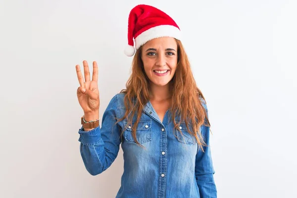 年轻美丽的红头发女人 头戴圣诞帽 头戴孤立的背景 带着自信和快乐的笑容 三指一指 — 图库照片