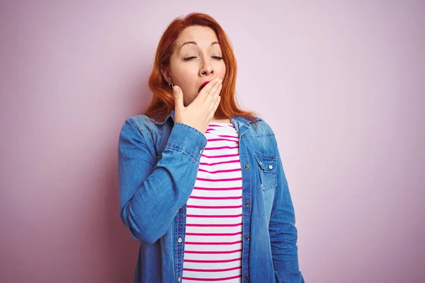 Beautiful redhead woman wearing denim shirt and striped t-shirt over isolated pink background bored yawning tired covering mouth with hand. Restless and sleepiness.
