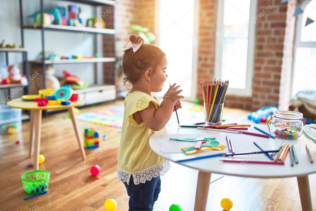 Beautiful toddler standing holding colored pencils at kindergarten