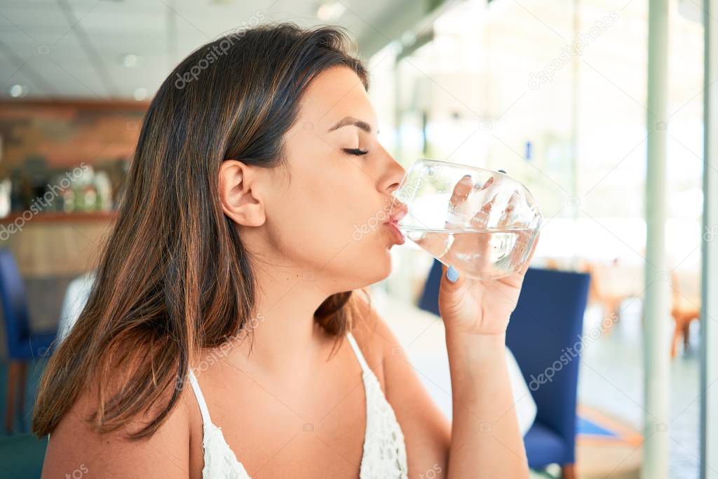 Young beautiful woman sitting at restaurant enjoying summer vacation drinking glass of water