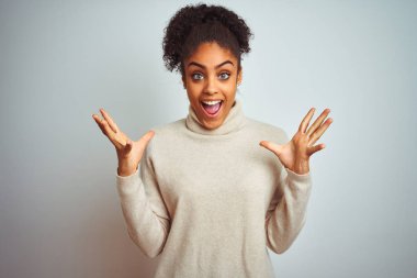 Kışlık balıkçı yaka kazak giyen Afro-Amerikalı kadın çılgın ve başarısını kutluyor. Kolları havada ve gözleri açık, heyecanlı bir şekilde çığlık atıyor. Kazanan konsept