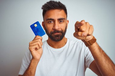 Genç Hintli müşteri kredi kartı tutuyor. İzole edilmiş beyaz arka plan üzerinde duruyor. Kamerayı işaret ediyor ve sen, el işareti, ön taraftan pozitif ve kendinden emin bir hareket.