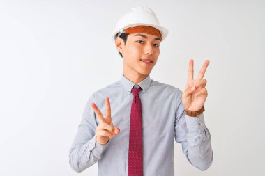 Kravat ve miğfer takan Çinli mimar izole edilmiş beyaz arka planda durup kameraya bakıp zafer işareti yaparken gülümsüyor. İki numara..