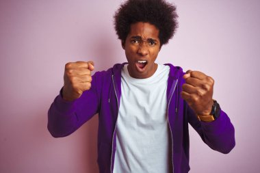 Mor eşofman üstü giyen genç Afro-Amerikalı adam öfkeyle bağırırken öfkeli ve öfkeli bir şekilde pembe arka planda dikiliyor. Öfke ve agresif kavram.