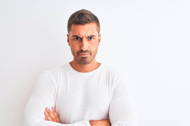 İzole edilmiş arka planda beyaz gömlek giyen genç yakışıklı adam şüpheci ve gergin, yüzünde çapraz kollu tasvip etmeyen ifade. Negatif kişi.