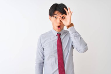 Soyutlanmış beyaz arka planda duran zarif kravat takan Çinli işadamı şaşırmış yüz ifadesiyle şaşırmış, parmaklarının arasından bakan bir jest yapıyor. İnançsız ifade.