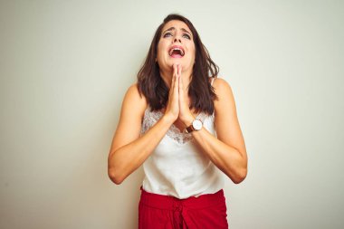 İzole edilmiş beyaz arka plan üzerinde duran tişört giyen genç ve güzel bir kadın elleri bağlı yalvarıyor ve dua ediyor. Yüzünde umut ifadesi var. Çok duygusal ve endişeli. Af diliyor. Din kavramı.