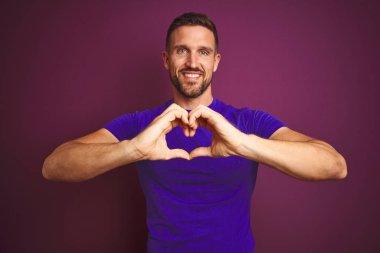Leylak rengi tişört giyen genç bir adam, izole edilmiş arka planda aşkla gülümsüyor, elleriyle kalp sembolü çiziyor. Romantik konsept.