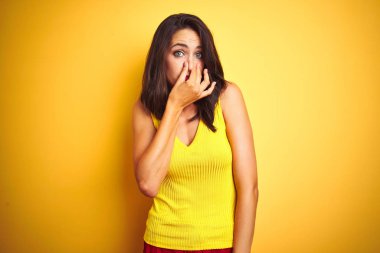 Sarı arka plan üzerinde duran tişört giyen genç güzel bir kadın pis ve iğrenç bir koku alıyor, dayanılmaz bir koku, parmakları burnunda nefesini tutuyor. Kötü koku konsepti.