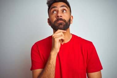 İzole edilmiş beyaz arka plan üzerine kırmızı tişört giyen genç Hintli bir adam. Elleri çenesinde soru sorarken, düşünceli bir ifade takınıyor. Düşünceli bir yüzle gülümsüyor. Şüphe kavramı.