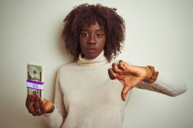 Kızgın yüzüyle izole edilmiş beyaz arka planda dolarları elinde tutan Afrikalı genç bir kadın. Negatif işaretler baş parmakları aşağıda, reddedilme konsepti ise reddedilmiş.