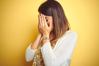 Sarı arka plan üzerinde duran ceketli genç ve güzel bir kadın. Ağlarken suratını ellerle kapatan üzgün bir ifade. Depresyon kavramı.