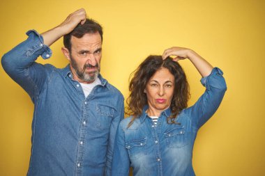 Güzel bir orta yaşlı çift, izole edilmiş sarı arka planda dikiliyorlar. Kafaları karışıyor ve soru soruyorlar. Şüpheyle kararsız, kafa kafaya düşünerek. Düşünceli kavram.