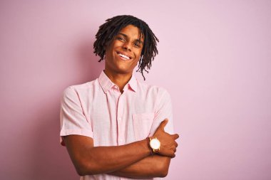 Zarif tişörtlü Afro-Amerikan bir adam izole edilmiş pembe arka planda duruyor ve kollarını kavuşturup kameraya bakıyor. Pozitif kişi.