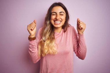 Young beautiful woman wearing a sweater over pink isolated background excited for success with arms raised and eyes closed celebrating victory smiling. Winner concept.