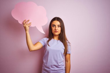 Genç, güzel bir kadın, pembe arka plan üzerinde bulutlu bir konuşma balonu tutuyor. Zeki bir yüz ifadesiyle ciddi olduğunu düşünüyor.