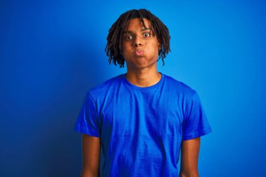 Rastalı tişörtlü Afro-Amerikalı adam izole edilmiş mavi arka planda duran komik yüzlü, şişkin yanaklı adam. Havayla şişmiş ağız, çılgın bir ifade..