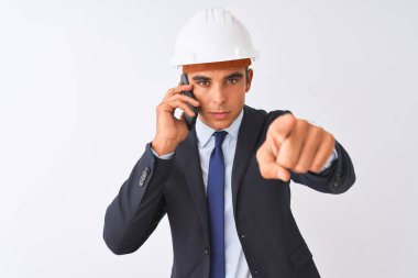 Miğfer takan genç mimar, akıllı telefondan konuşan, izole edilmiş beyaz arka planda, kamerayı işaret eden, el işareti, ön taraftan olumlu ve kendinden emin bir hareket.