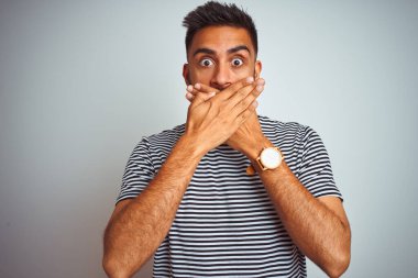 Siyah çizgili tişört giyen genç Hintli adam izole edilmiş beyaz arka planda dikiliyor ağzı yanlışlıkla ellerle kapatıyor. Gizli konsept.