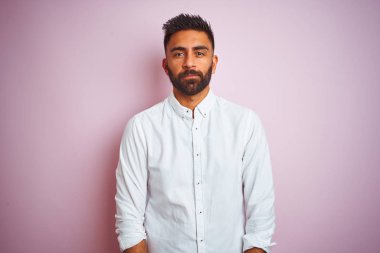 Soyutlanmış pembe arka planda duran zarif gömlekli genç Hintli işadamı yüzünde ciddi bir ifadeyle rahatlamış. Basit ve doğal bir şekilde kameraya bakıyorsun..