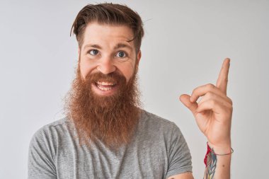 Genç, kızıl saçlı, tişörtlü bir adam gri arka planda dikiliyordu. Elleri ve parmakları kenarda mutlu bir şekilde duruyordu.