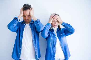 Young beautiful couple wearing denim shirt standing over isolated white background suffering from headache desperate and stressed because pain and migraine. Hands on head.