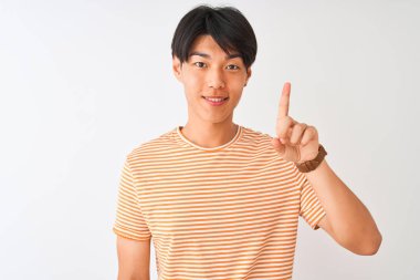 Sıradan çizgili tişört giyen genç Çinli bir adam izole edilmiş beyaz arka planda duruyor ve bir numarayı işaret ederken kendinden emin ve mutlu bir şekilde gülümsüyor..