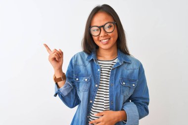 İzole edilmiş beyaz arka plan üzerinde kot gömlek ve gözlük takan genç Çinli bir kadın. Yüzünde kocaman bir gülümseme, eli ve parmağı kameraya bakıyor..