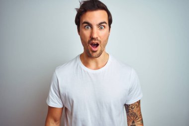 İzole edilmiş beyaz arka plan üzerine sıradan tişörtler giyen yakışıklı genç bir adam korku, korku ve heyecan dolu bir yüz ifadesiyle dehşete düşmüş ve şok olmuştu..