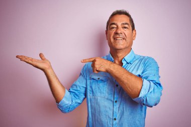 Mavi kot giyen yakışıklı orta yaşlı bir adam soyutlanmış pembe arka planda duruyor.