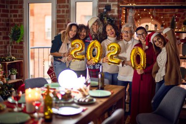 Mutlu ve kendinden emin gülümseyen güzel bir kadın grubu. Evde 2020 balon tutan noel ağacı etrafında poz vermek
