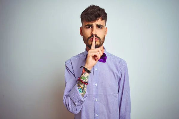 有纹身 穿紫色衬衫 打着领结 罩在孤立的白色背景上的年轻人要求安静 手指放在嘴唇上 沉默和秘密概念 — 图库照片
