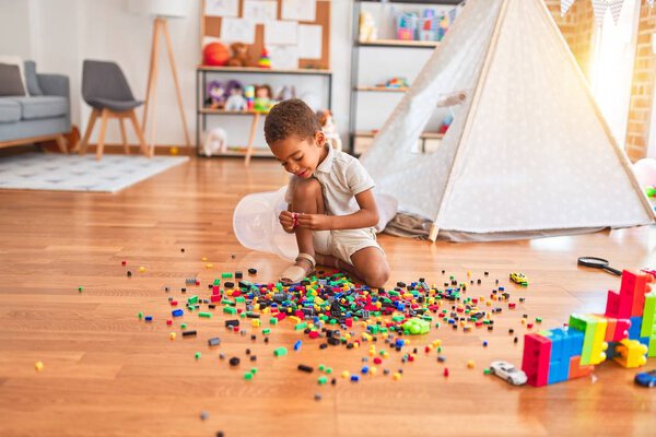 Beautiful african american toddler playing with small building blocks smiling at kindergarten