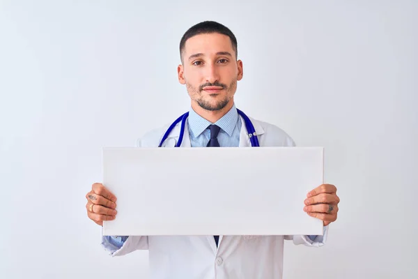 年轻的医生拿着空白的广告横幅在孤立的背景上 脸上带着自信的表情 严肃地思考着 — 图库照片
