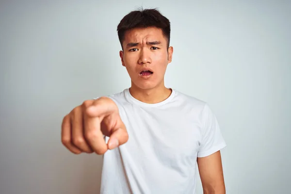 穿着T恤衫的年轻的亚裔男子站在与世隔绝的白色背景上 对着摄像机表示不满和沮丧 对你感到愤怒和愤怒 — 图库照片