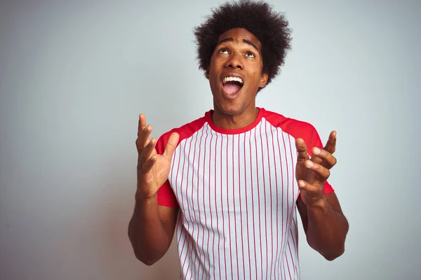 African american man with afro hair wearing red striped t-shirt over isolated white background crazy and mad shouting and yelling with aggressive expression and arms raised. Frustration concept.