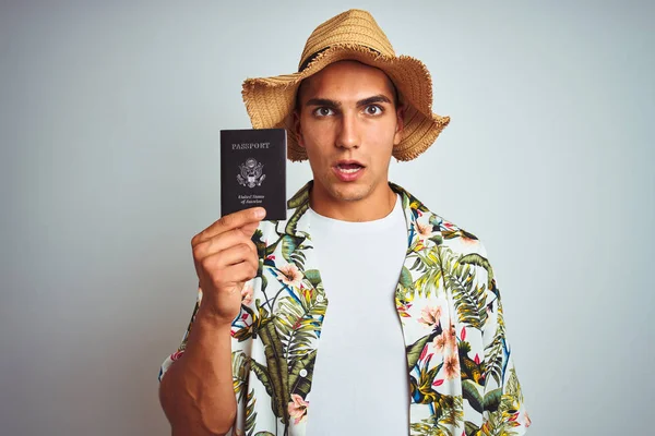 Young handsome man holding United States passport over white isolated background scared in shock with a surprise face, afraid and excited with fear expression