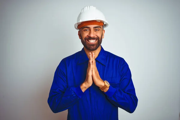 手で一緒に祈っている孤立した白い背景に制服とヘルメットを身に着けているハンサムなインドの労働者は 自信を持って笑顔許しを求めて — ストック写真
